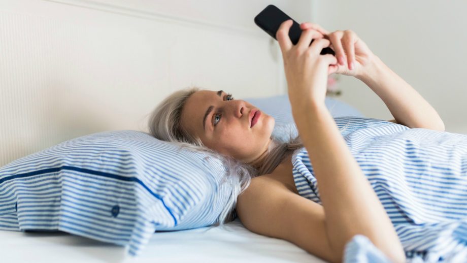 Image of girl laying in bed, holding phone above her to see phone screen.